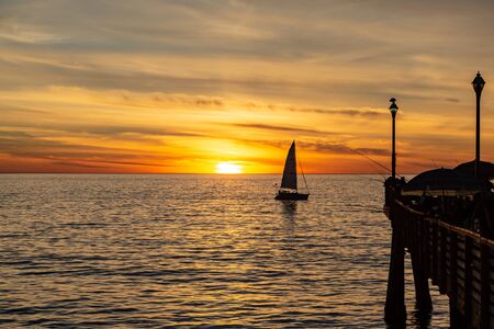The pier at Redondo Beach in California, and a silhouetted sailing boat, at sunsetの写真素材