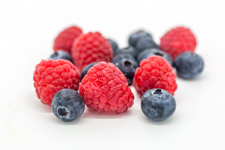 Healthy raspberries and blueberries against a white background