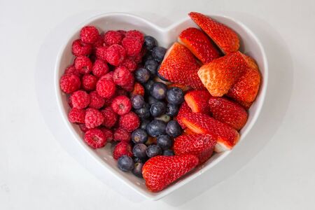 Raspberries, Blueberries and Strawberries in a Heart Shaped Bowlの写真素材