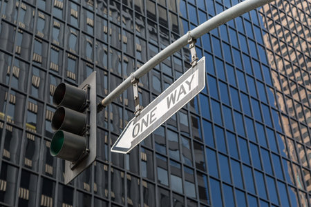 Looking up at a One Way sign and traffic lights, with buildings behind