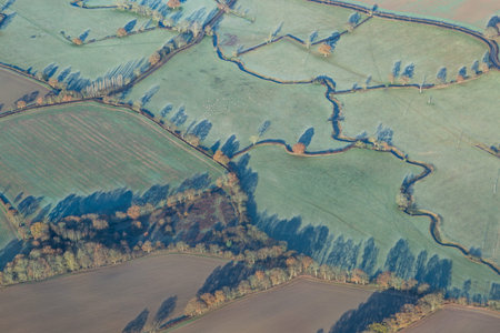 Looking down over Sussex fields during early morning in winter, with long shadows of trees over fields, taken from the flightdeck of an airplane.の写真素材