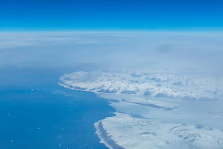 A view of a snowy landscape of Greenland, taken from the flight deck of an airplaneの写真素材