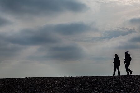 Silhouetted people on a pebble beach in wintertimeの写真素材