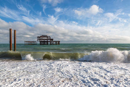 Waves crashing in front of the ruins of the West Pier in Brighton, with a blue sky overheadの写真素材
