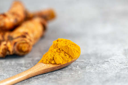 A spoonful of ground turmeric with turmeric root defocused behindの写真素材