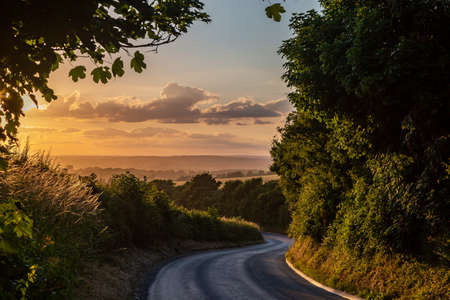Looking along a county road in rural Sussex with a sunset sky over the distant fieldsの写真素材
