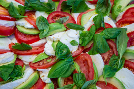 A summer salad of tomato, mozzarella, avocado and basil leavesの写真素材