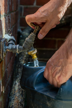 A man filling a watering can from an outside tap during a hosepipe ban in the UK