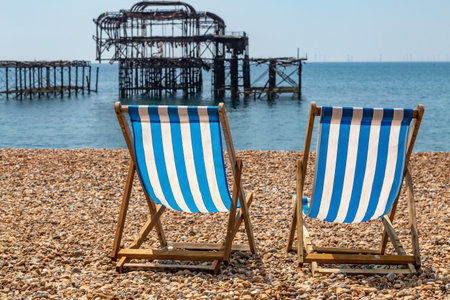 A close up of two deck chairs on Brighton Beach, with a defocused West Pier behind