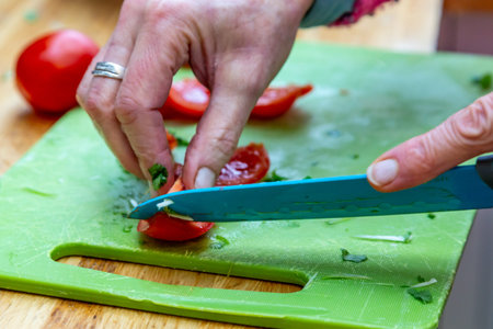A womans hand holding a knife and chopping a tomatoの写真素材