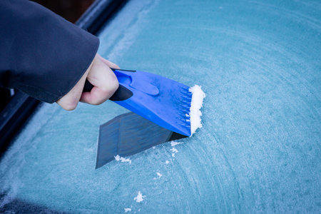A close up of a man scraping ice from a car windscreen on a winter's day