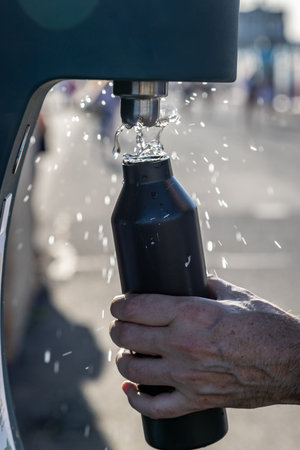 A hand holding a water bottle and refilling it from an outside water fountain, with a shallow depth...