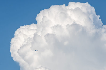 Looking up at a large fluffy cloud with a blue sky behind, and an airplane passing in front
