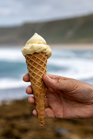 A close up of a vanilla ice cream being held, with the ocean defocused behind
