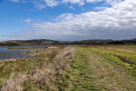 A view along a grass pathway running alongside a lake in Lewes wetlandsの写真素材
