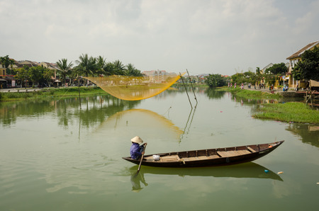 Hoi An, Vietnam, February 10, 2015 - Vietnamese woman paddles a traditional boat on the Thu B?n River. A net to catch fish is suspended on poles in the middle of the river.のeditorial素材