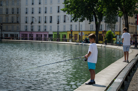 Paris, France, August 7, 2015 - Two boys are fishing in the Canal Saint-Martin on a hot summer day. Galleries, cafes and shops line Quai de Valmy alongside the water.のeditorial素材