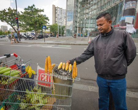 PARIS - FRANCE SEPTEMBER 3, 2015: Man cooks corn on the cob over coals on a makeshift stove in a shopping cart outside of a mall at Place d'Italie.のeditorial素材