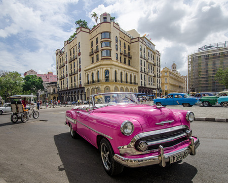 HAVANA - CUBA. JUNE 10, 2016: Close-up of a hot pink restored classic convertible drives along Paseo de Marti with the Parque Central Hotel and the historic Plaza Hotel in the background.のeditorial素材