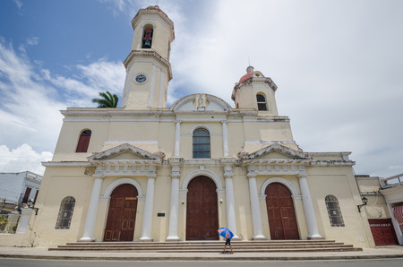 Cienfeugos, Cuba,  June 15, 2016 - A woman walks by the Catedral de la Purisma Concepcion that dominates Plaza Jose Marti. She protects herself from the hot sun with an umbrella.のeditorial素材
