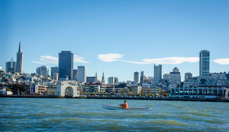 San Francisco, United States, December 2, 2016 - A lone man rows in a small boat in chilly winter waters of the San Francisco Bay with the city skyline in the background.のeditorial素材