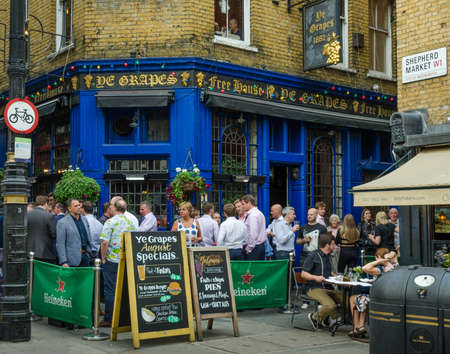 London, England, August 18, 2018 - : Patrons of the Ye Grapes, a tavern in the Mayfair district spill out into the streets on a Friday evening, meeting friends at the end of the work week.のeditorial素材