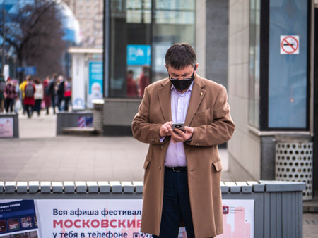 Russia Moscow 2021. A view of a man in the city standing on the street in a medical mask and looking at his mobile phone. Coronavirus wave in Moscow in autumn 2021のeditorial素材