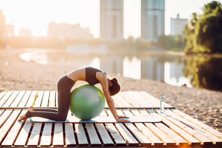 Sportswoman do yoga with fitness ball at sunriseの写真素材