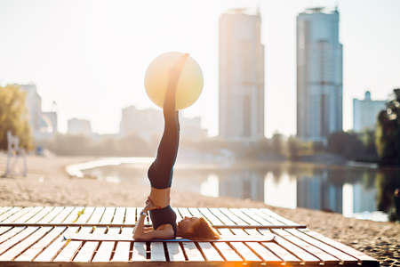 Sportswoman do yoga with fitness ball at sunriseの写真素材
