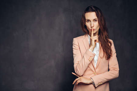 Adult woman show silence sign on dark backgroundの写真素材