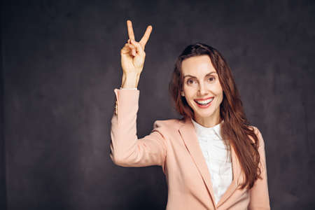 Adult woman show victory sign on dark backgroundの写真素材