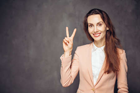 Adult woman show victory sign on dark backgroundの写真素材