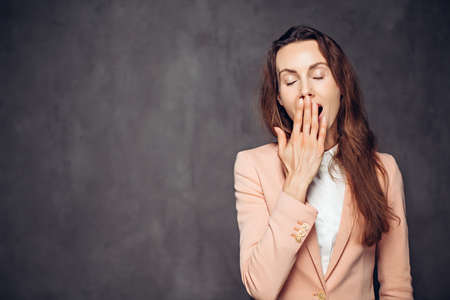 Adult caucasian woman yawning on dark backgroundの写真素材