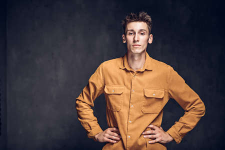 young man with hands on hips on dark backgroundの写真素材