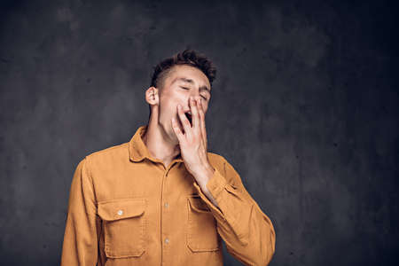 young caucasian man yawning on dark backgroundの写真素材