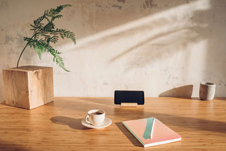 Desk with a smartphone, notebook and cup of coffee in sunlightの写真素材