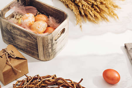 A simple rural composition. Painted in pastel warm colors Easter eggs in a wooden box in sunlight on a white table near the windowの写真素材