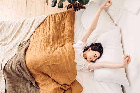 Lifestyle portrait of a happy young girl waking up and stretching in bed early in the morningの写真素材