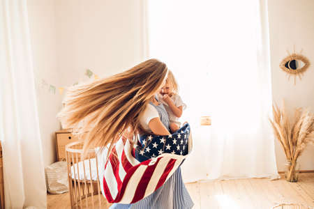 Young mother or babysitter with a little girl in her arms spin in the middle of the room celebrating July 4th Independence Dayの写真素材