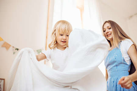 A little girl helps her mother to make the bed. They play and have fun at homeの写真素材