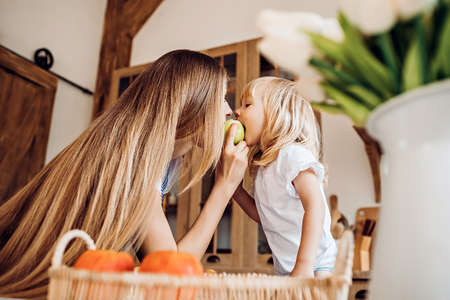Little girl treats her mother to an apple at the kitchenの写真素材