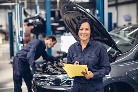 Auto car repair service center. Two mechanics - man and woman examining car engineの写真素材
