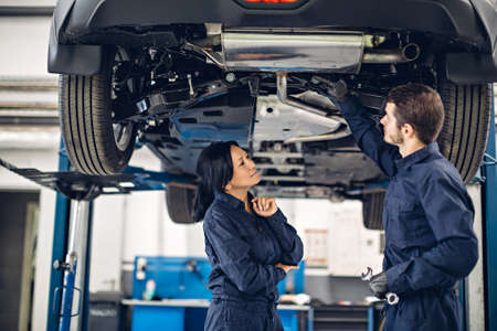 Auto car repair service center. Two mechanics - man and woman examining carの写真素材