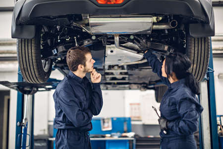 Auto car repair service center. Two mechanics - man and woman examining carの写真素材