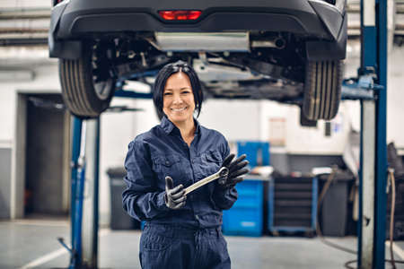 Auto car repair service center. Happy female mechanic standing by the carの写真素材