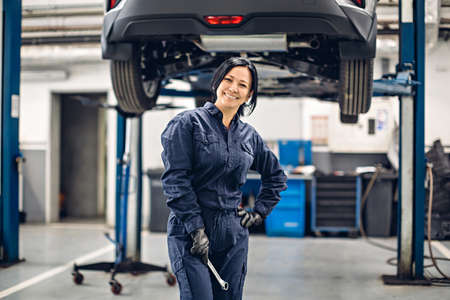 Auto car repair service center. Happy female mechanic standing by the carの写真素材