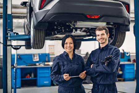 Auto car repair service center. Two happy mechanics - man and woman standing by the carの写真素材