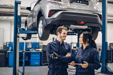 Auto car repair service center. Two happy mechanics - man and woman standing by the carの写真素材