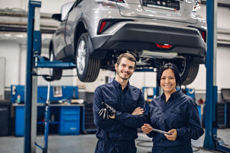 Auto car repair service center. Two happy mechanics - man and woman standing by the carの写真素材