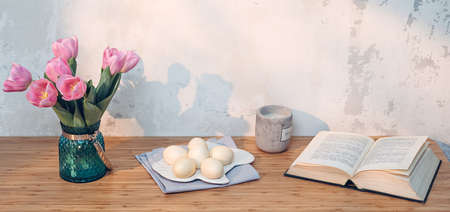 Easter eggs, book and pink tulips on table. Simple holiday imageの写真素材